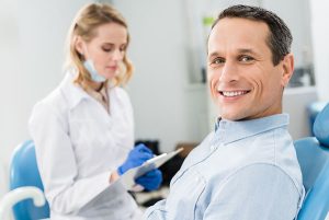 Man smiling in a dental chair while a dental professional notes information, emphasizing patient care at MA's Family & Cosmetic Dentistry.
