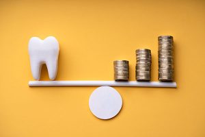 Tooth model balancing on a scale with stacks of coins, illustrating the value of professional mouthguards in dental health investment.
